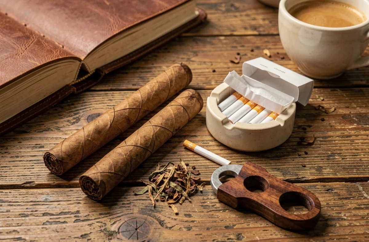 Comparaison visuelle entre un cigare artisanal et des cigarettes sur une table en chêne avec accessoires, illustrant les différences physiques entre les deux produits